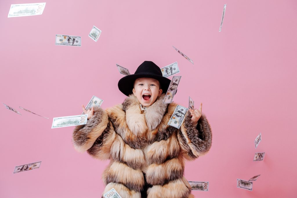 Smiling toddler in luxurious fur coat and hat in the rain of money richest kid in the world