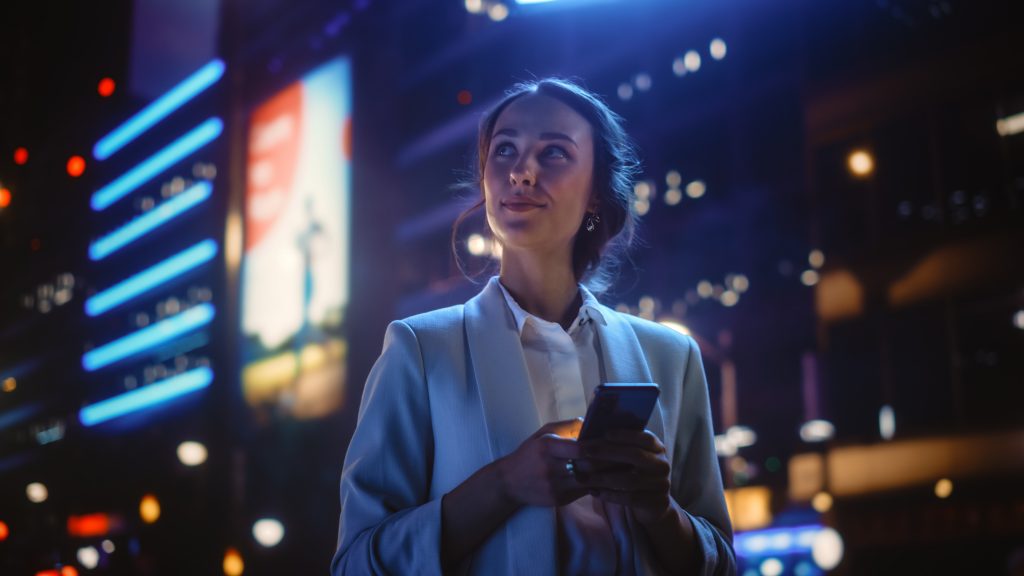Beautiful Young Woman Using Smartphone Standing on the Night Cit