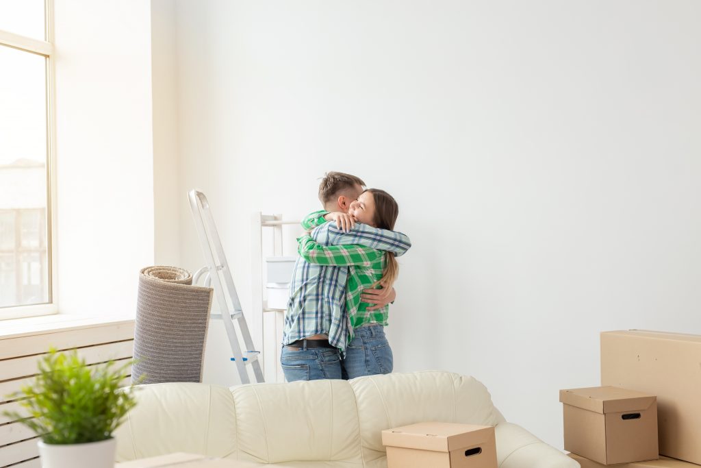 Unidentified young couple embraces and dances in the living room of their new apartment. The concept of affordable mortgage and new housing for a young family