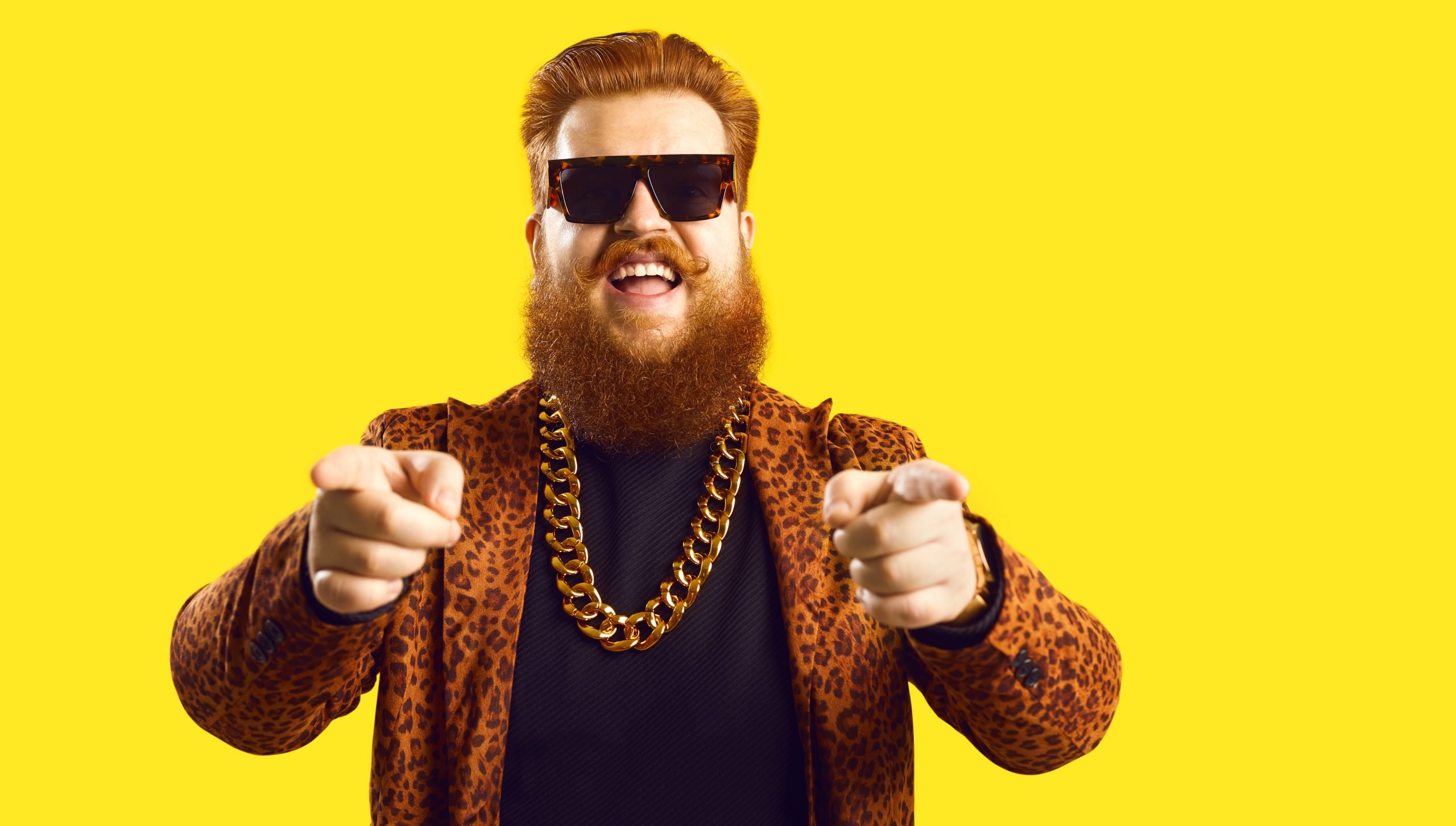 Man in gold chain and funky suit pointing fingers at camera isolated on color background