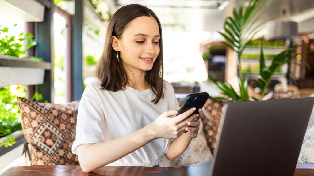 freelance young woman sitting cafeteria with laptop and smartphone using cloud hosting service