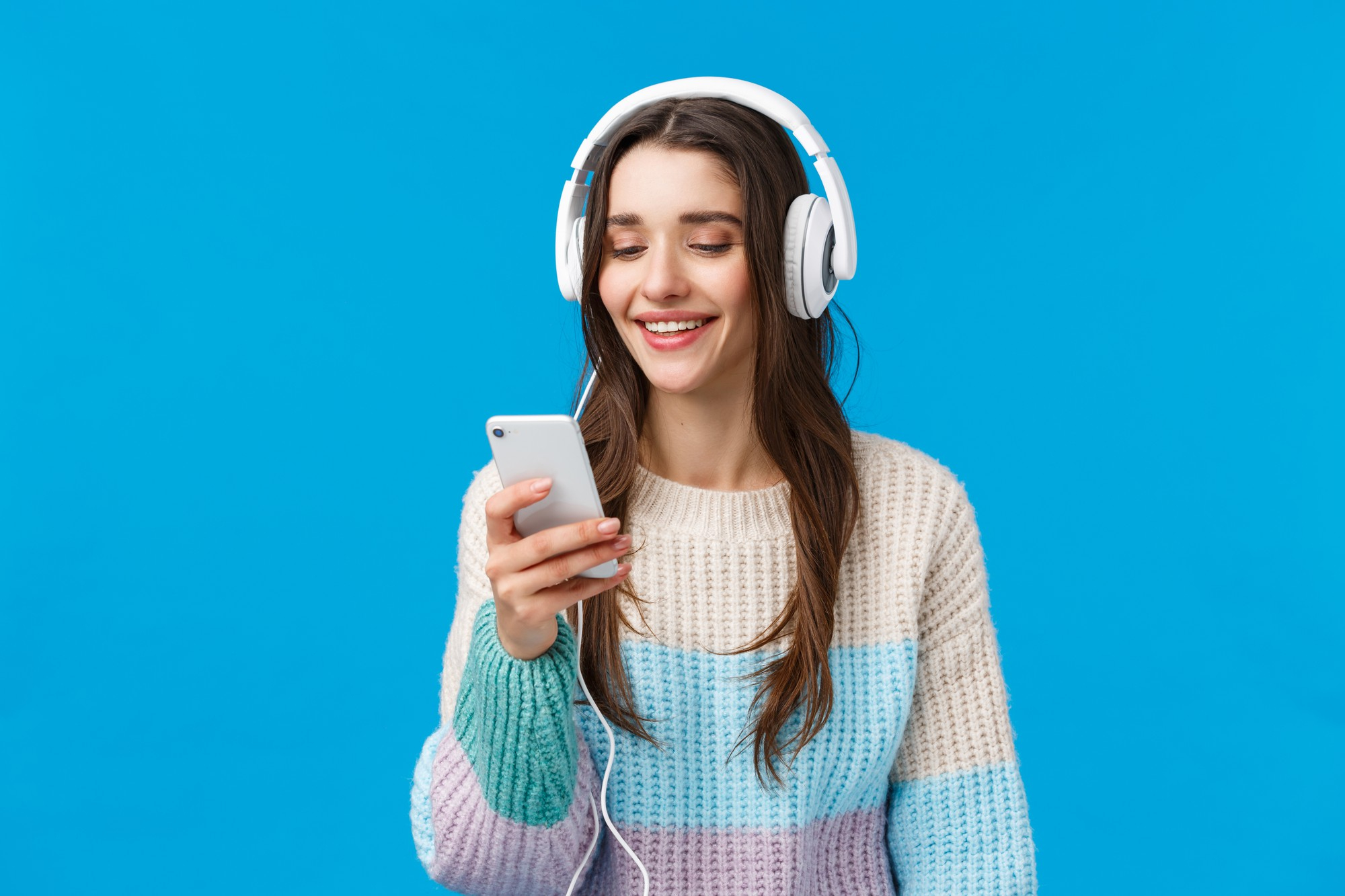 young millennial woman with headphones using streaming music app on cellphone blue background