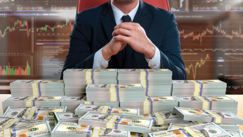 businessman sitting with pile of 100 dollar banknote