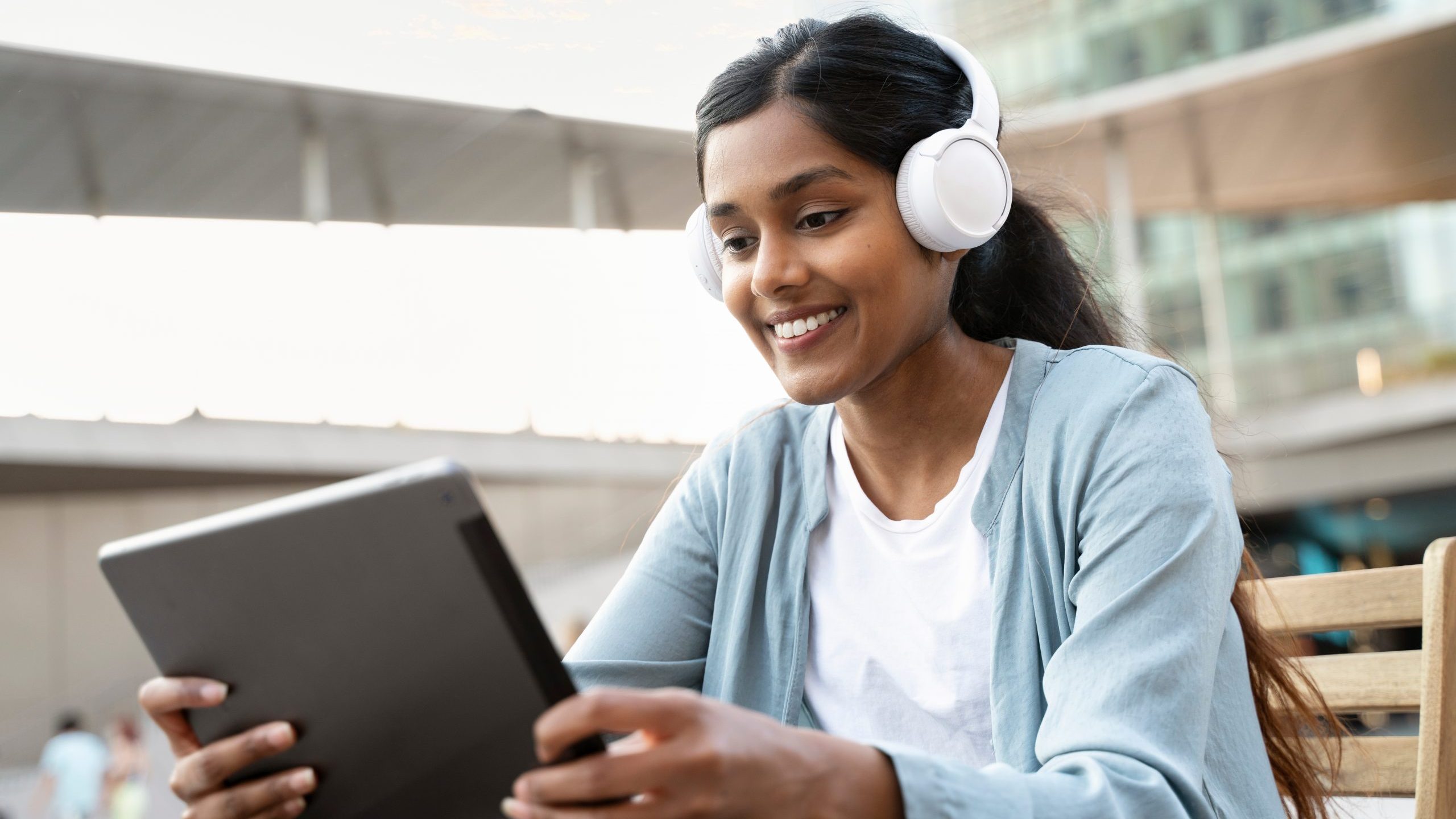 Smiling Indian woman wearing wireless headphones using digital t